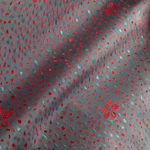 Close-up of fabric with red floral motifs on a blue-grey background, featuring small red and blue dotted patterns.