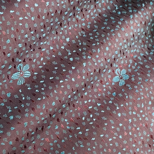 Close-up of maroon fabric with small white floral patterns and scattered white dots, highlighting its intricate design.