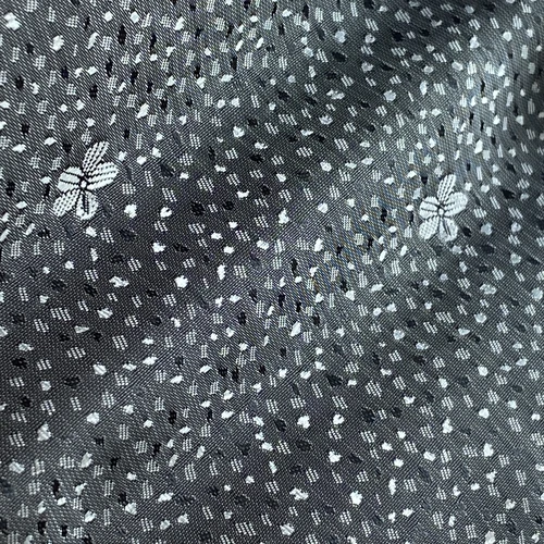 Intricate fabric pattern with white flowers and speckles on a gray background, creating a textured, elegant design.