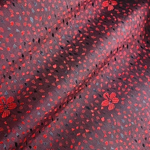 Red floral pattern fabric with small dots and flowers, creating a textured design. Perfect for textile projects.
