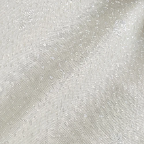 Close-up of a cream textured fabric with subtle dotted patterns and light reflection.