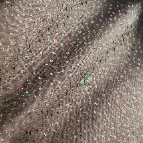 Close-up of pink textured fabric with intricate patterns and subtle floral embroidery, perfect for fashion or upholstery.