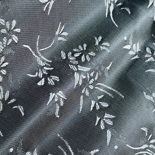Silky fabric with intricate white floral pattern on a soft gray background, showcasing elegant textile design.