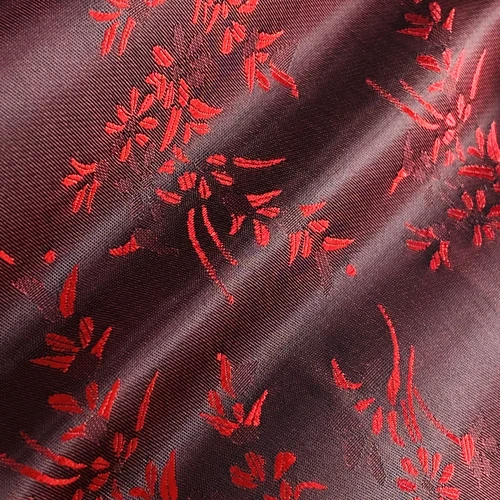 Closeup of luxurious red floral patterns on silky maroon fabric, showcasing elegant embroidery details.