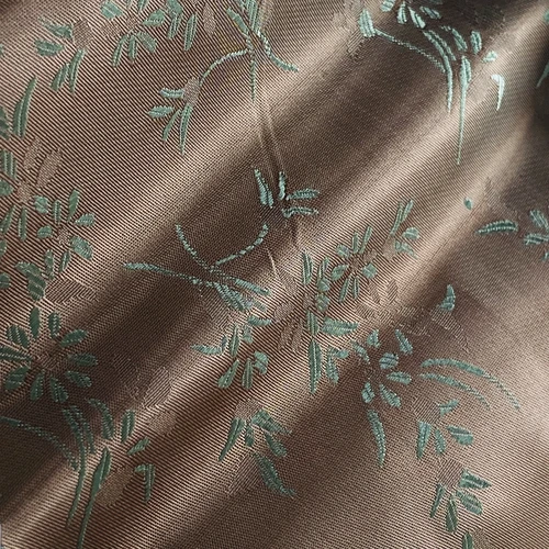Close-up of brown silk fabric with intricate teal floral embroidery pattern.