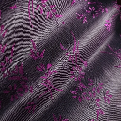 Elegant purple floral pattern on black silky fabric, close-up view showcasing intricate design and texture.
