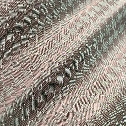 Close-up of textured brown and beige houndstooth fabric pattern under soft lighting, showcasing woven details.