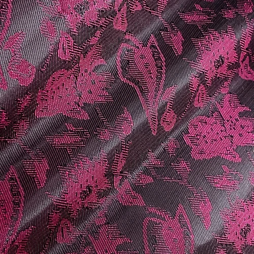 Close-up of intricate pink floral damask fabric pattern on a dark background, showcasing elegant textile design.