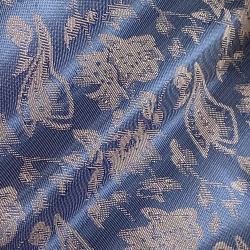 Close-up of blue fabric with intricate floral pattern, showcasing detailed embroidery and texture.