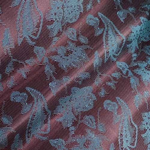 Close-up of fabric with intricate blue floral pattern on dusty pink background, highlighting texture and design details.