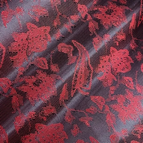 Rich red floral pattern on textured dark fabric, highlighting the intricate design and luxurious material.