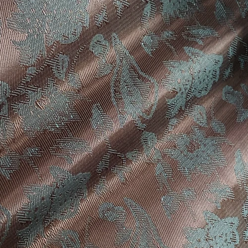 Close-up of jacquard fabric with intricate floral patterns in teal on a brown background.