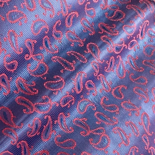 Close-up of blue and pink paisley fabric texture with intricate embroidered patterns shining under light.