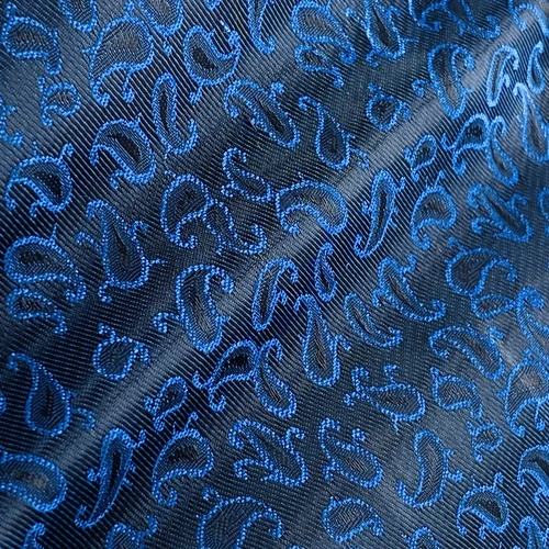 Close-up of a textured fabric with a blue paisley pattern on a dark background, highlighting its intricate design.