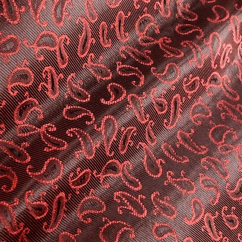 Red paisley embroidery on dark fabric, showcasing intricate patterns and luxurious texture.