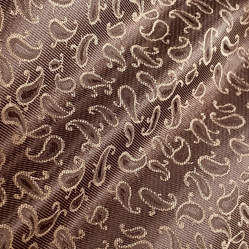 Close-up of brown fabric with an intricate paisley pattern, showcasing texture and detailed embroidery.
