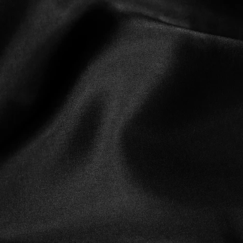 Smooth black fabric with gentle folds, showing texture and light reflections. Ideal for fashion and textile contexts.