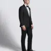 Man in a black tuxedo with bow tie, standing against a plain background for formal wear fashion.