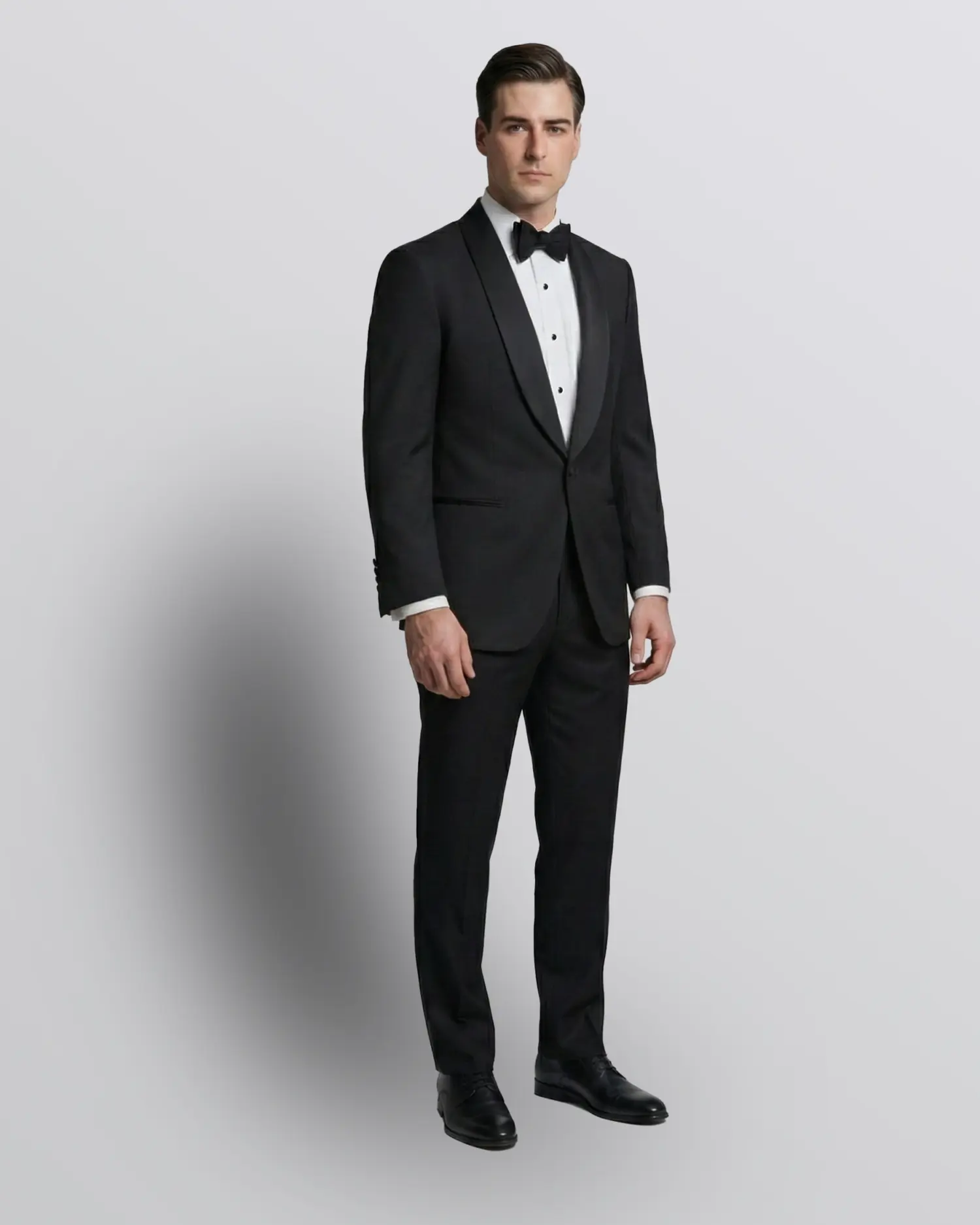 Man in a black tuxedo and bow tie, posing against a plain background, showcasing formal evening wear.