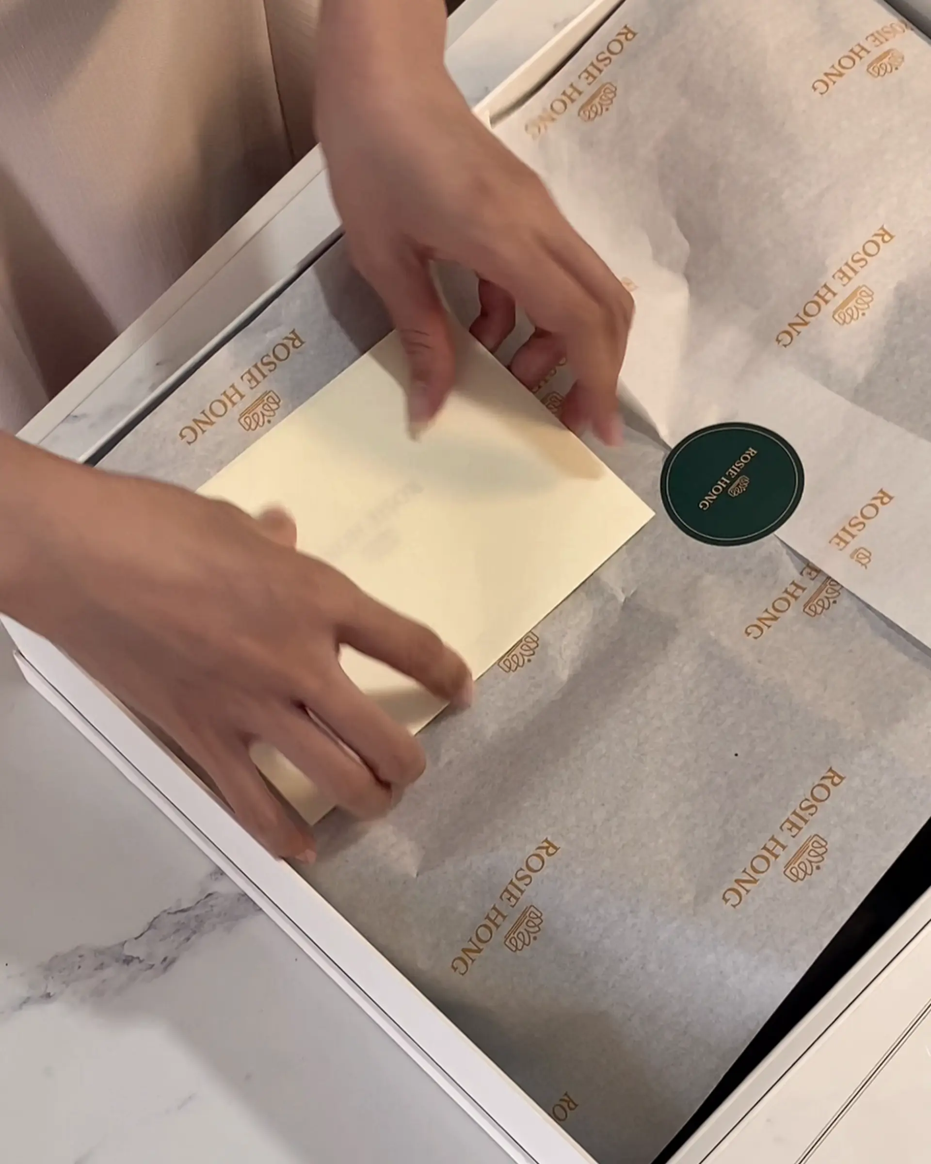 Person wrapping a gift box with branded paper and adding a personal note card.