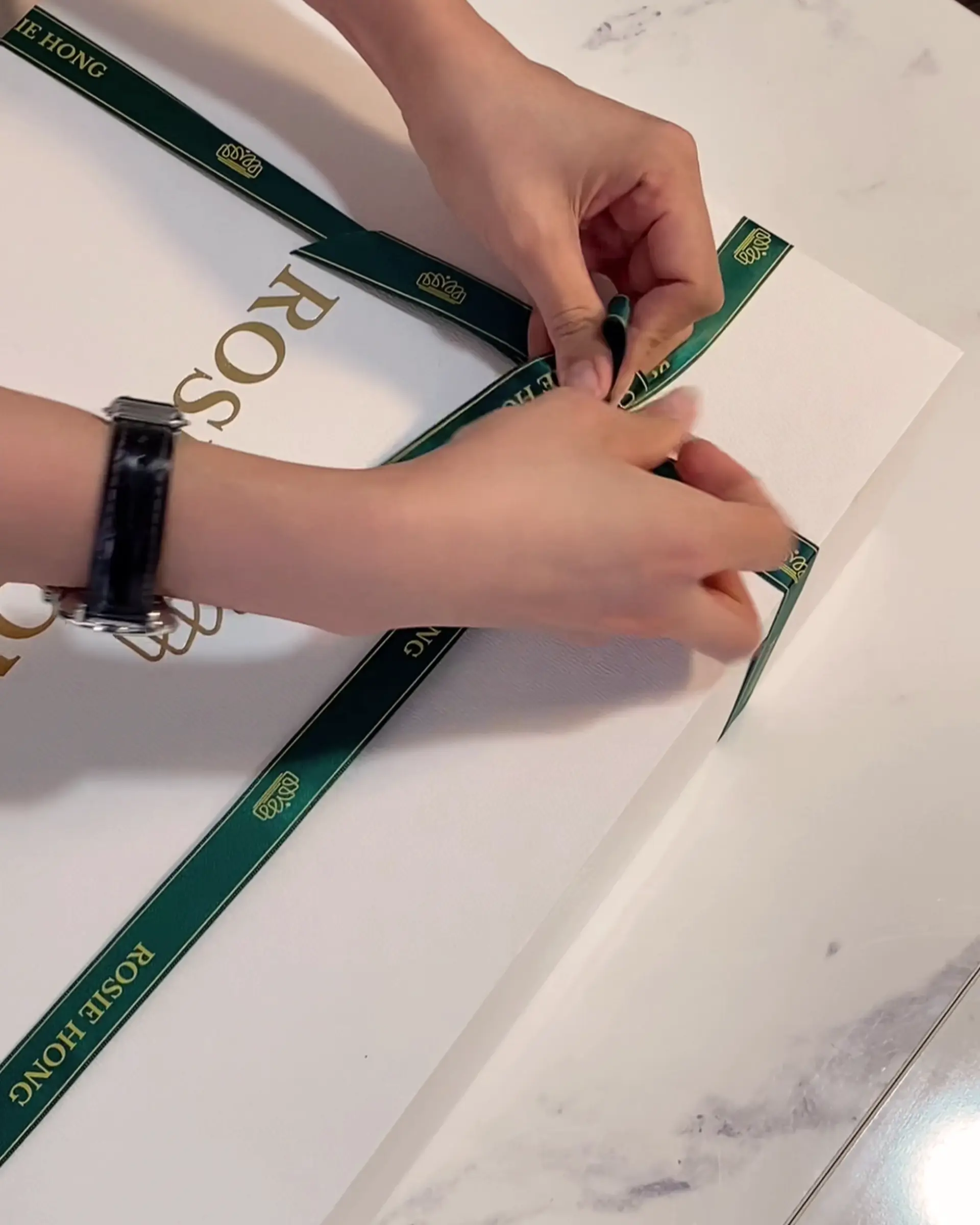 Hands tying a green ribbon on a white gift box, adding an elegant touch to luxurious packaging.