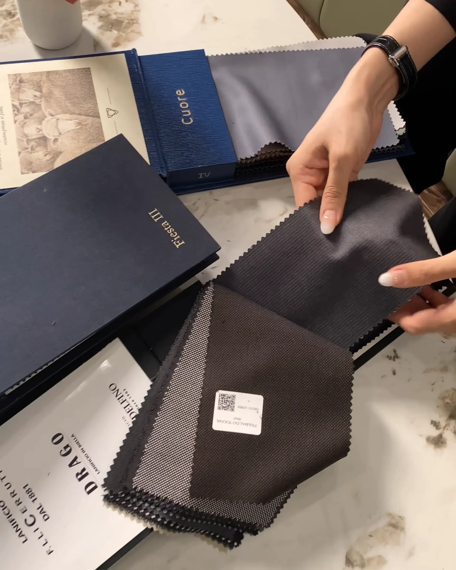 Person selecting fabric swatches from luxury textile sample books on a table.
