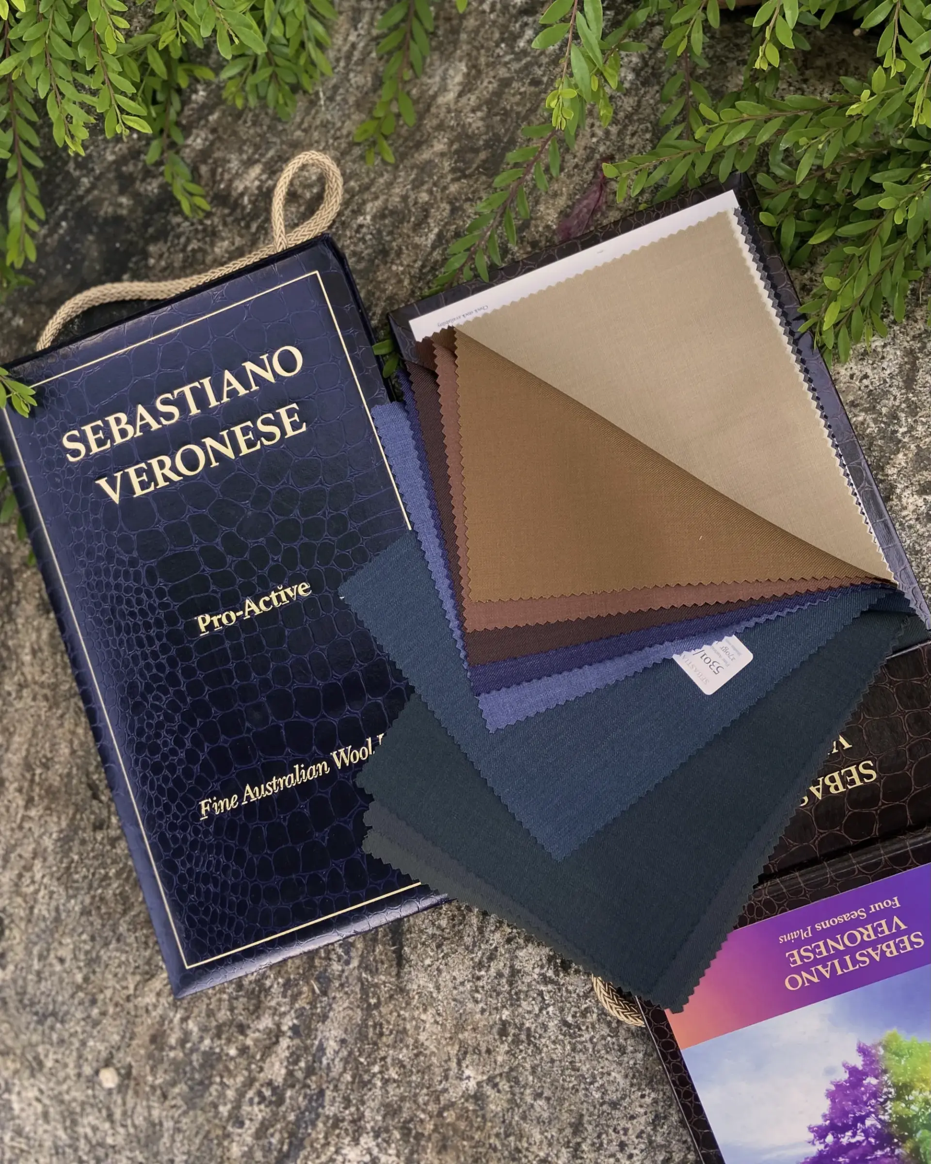 Fabric samples on textured surface with Sebastiano Veronese packaging, showcasing a variety of colors and textures.