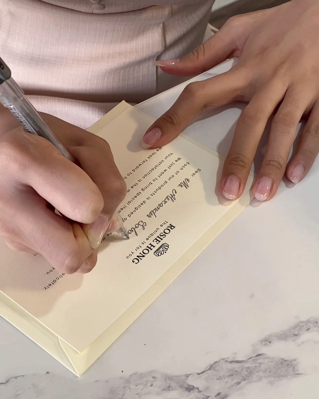 Person writing a note on letterhead with a pen on a marble table.