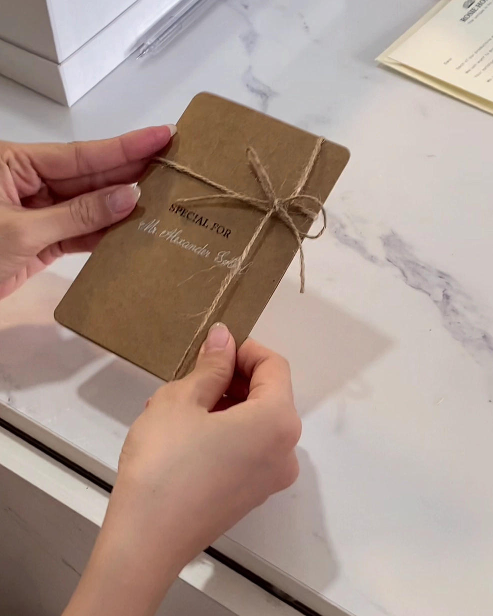 Hands holding a tied brown envelope labeled Special For Mr. Alexander Scott on a marble surface.