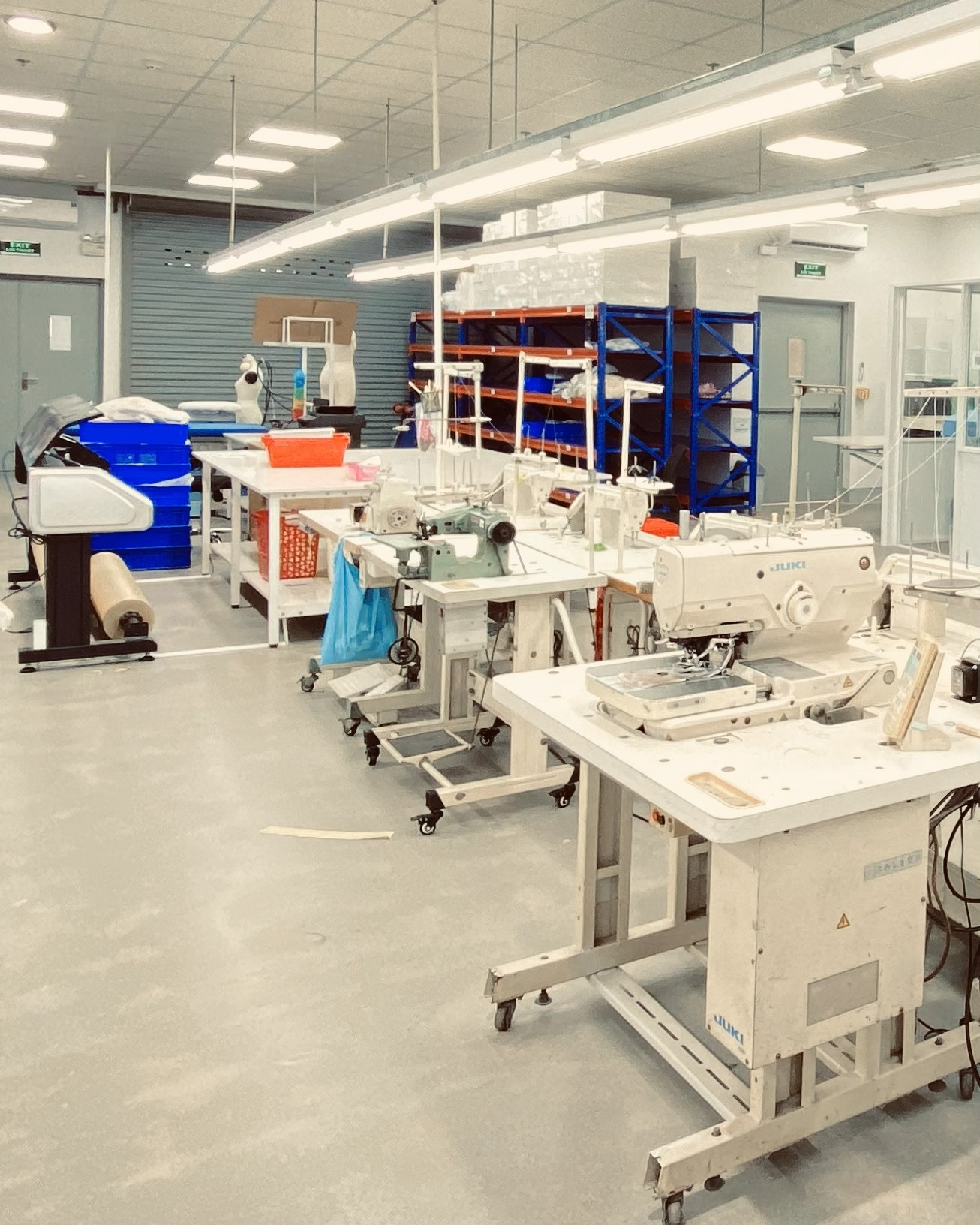 Industrial sewing equipment in a well-lit, modern textile factory workshop with tables and shelves.