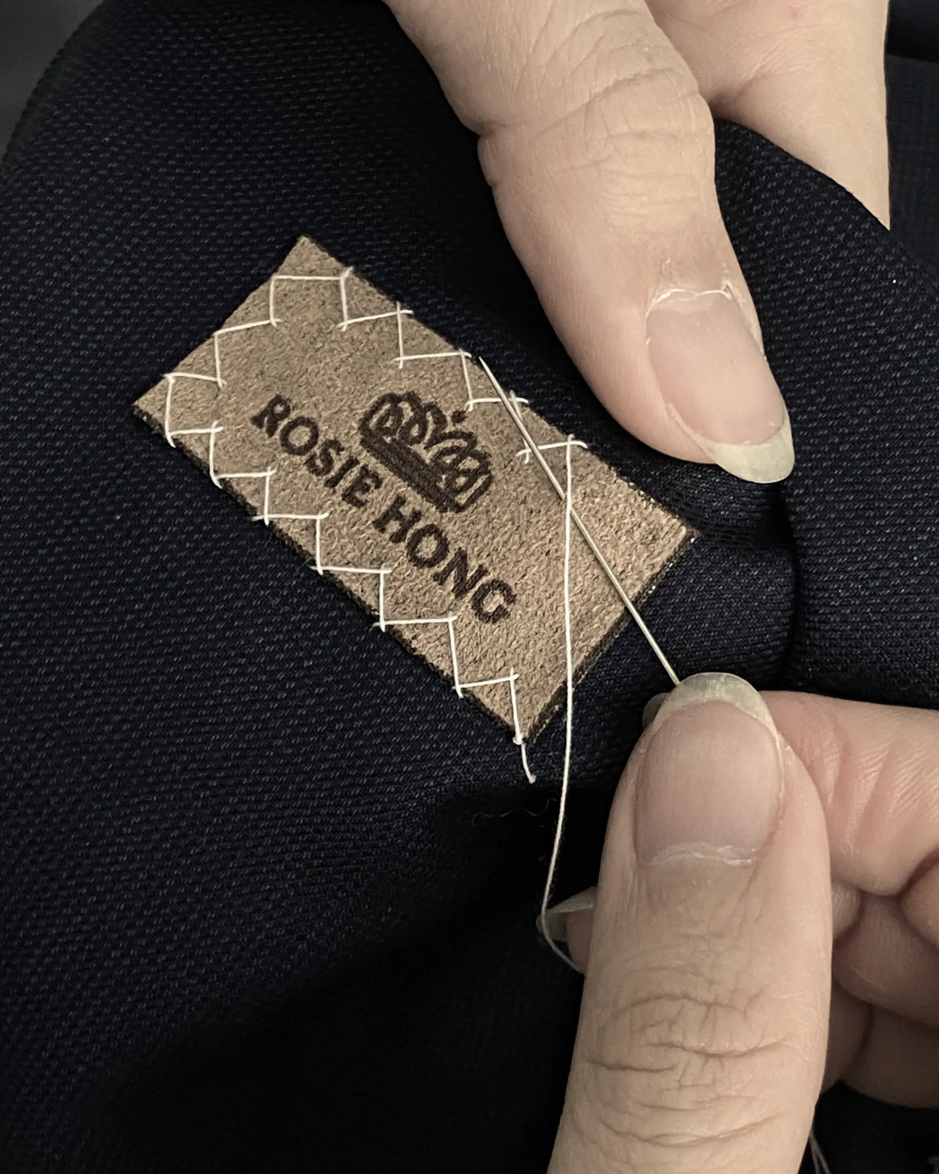 Sewing a Rosie Hong label onto fabric with needle and thread, showcasing craftsmanship and branding.