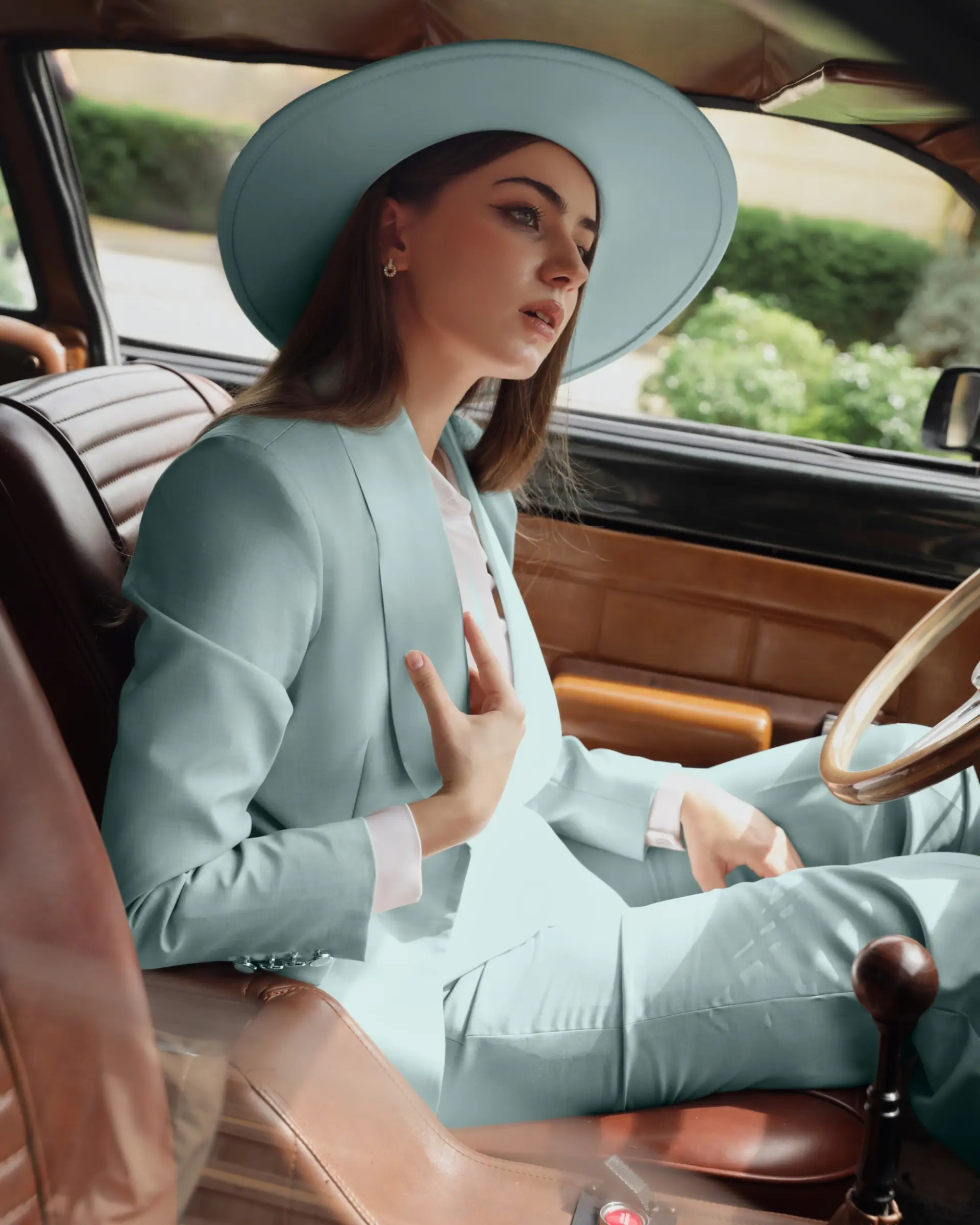 Woman in a stylish light blue suit and hat, sitting in a vintage car, expressing elegance and sophistication.