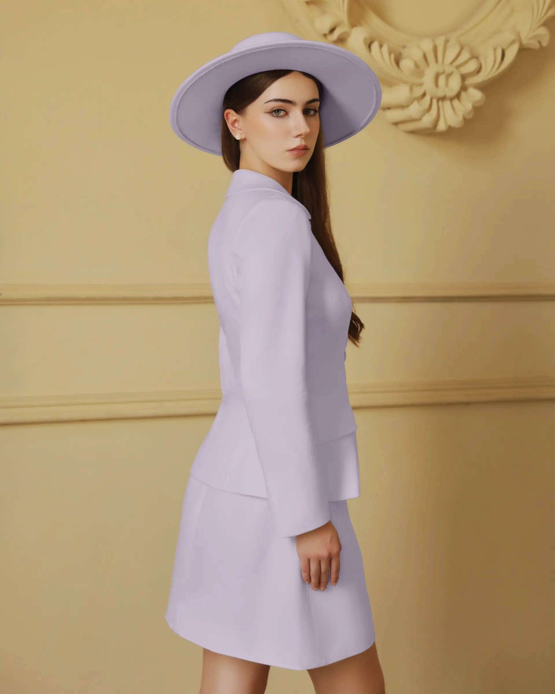 Woman in a lavender suit and hat, standing in a stylish beige room.