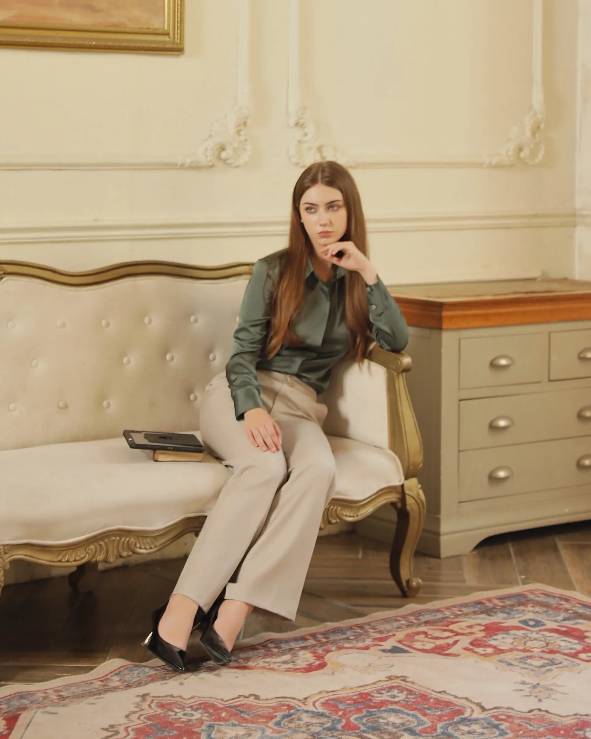 Woman sitting on vintage sofa in elegant room, contemplative pose, stylish attire, classic decor, fashion inspiration.
