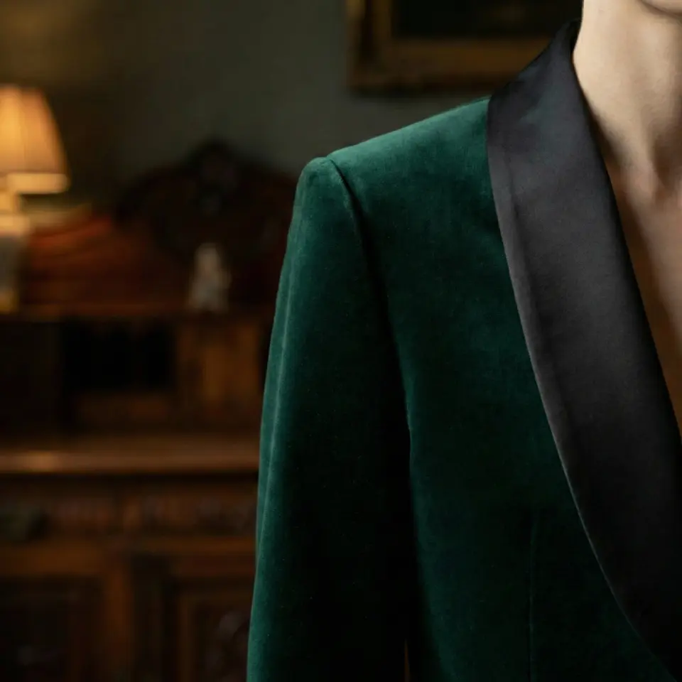 Elegant emerald velvet blazer with black satin lapel, set in a warm, vintage room ambiance.