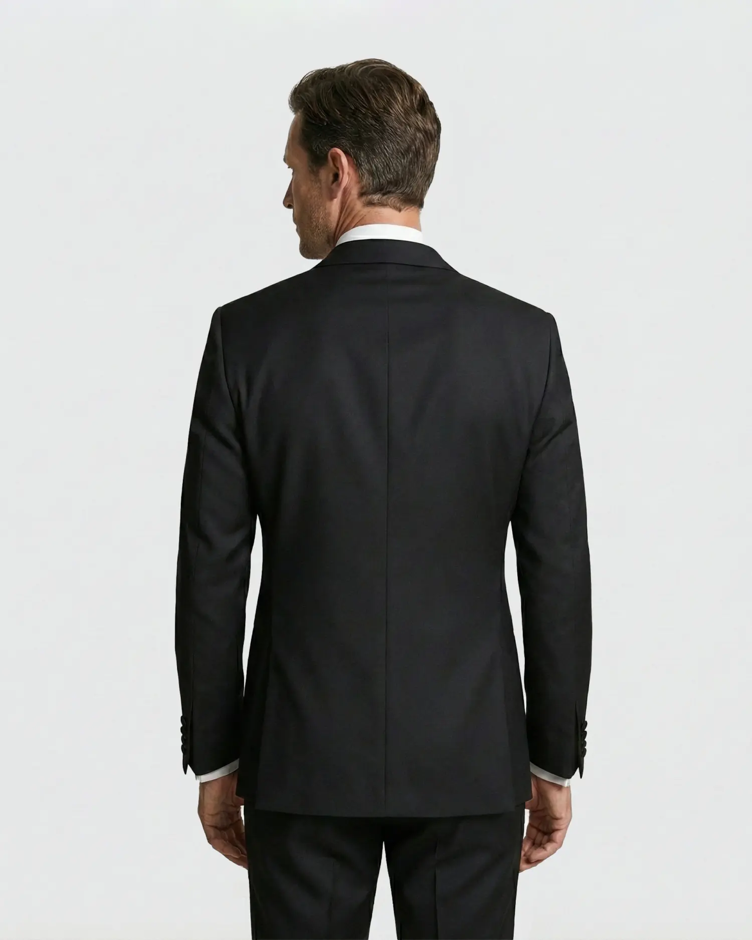 Back view of a man in a sleek black suit, showcasing elegant tailoring and style against a plain background.