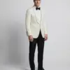 Man in a white tuxedo jacket and black bow tie standing against a plain background.