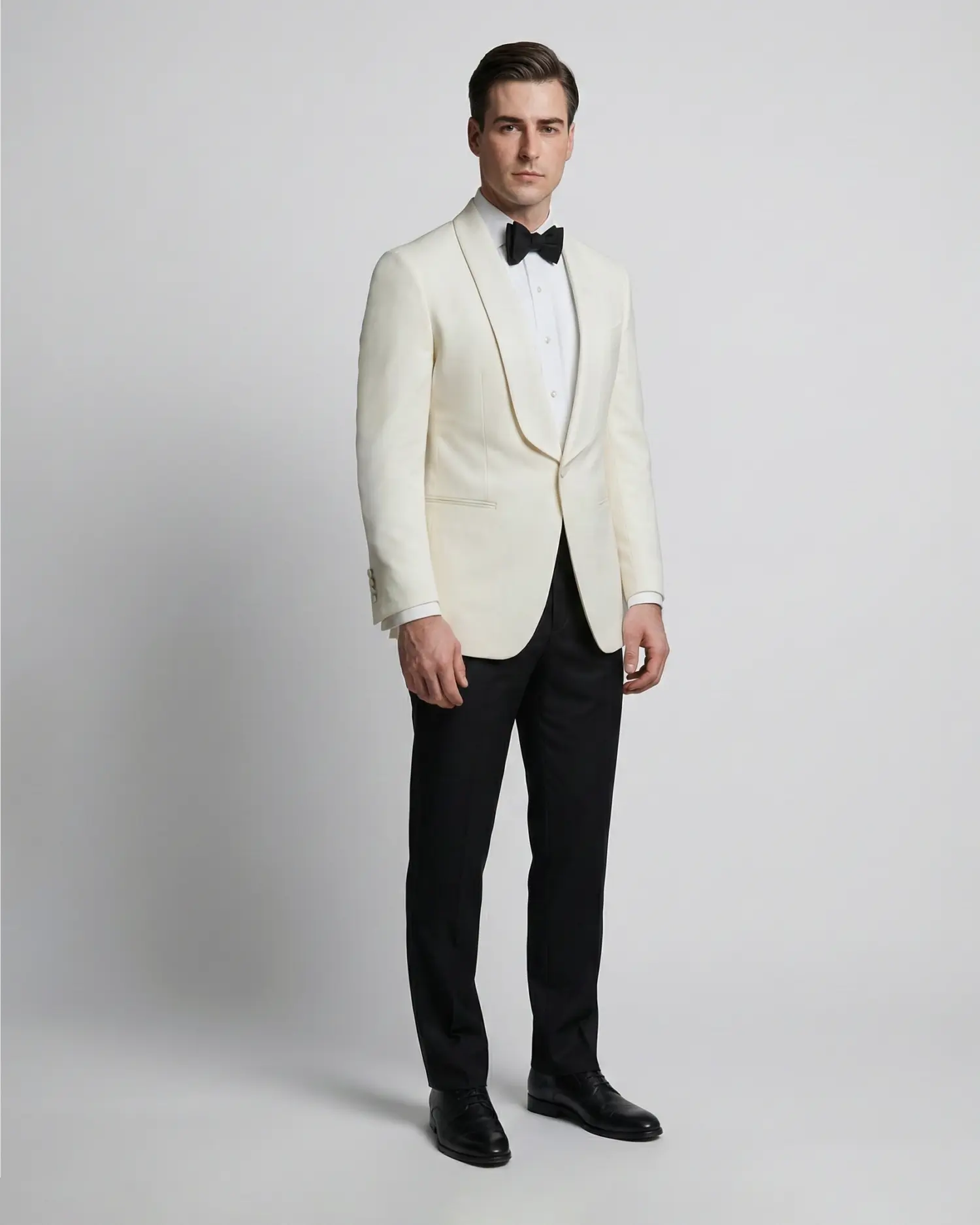 Man in a white tuxedo jacket and black bow tie standing against a plain background.