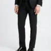 Man in a black suit with patent leather shoes, standing against a plain background.