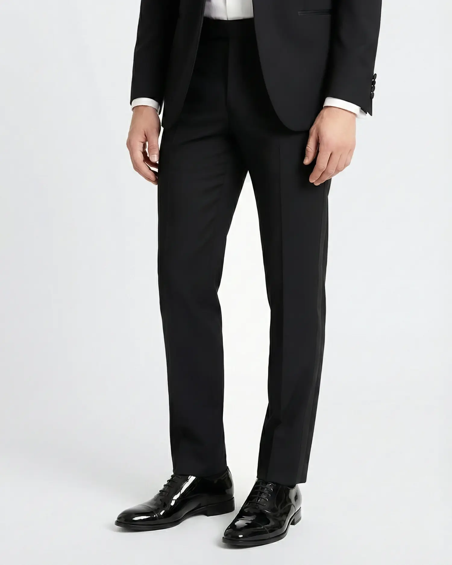 Man in a black suit with patent leather shoes, standing against a plain background.