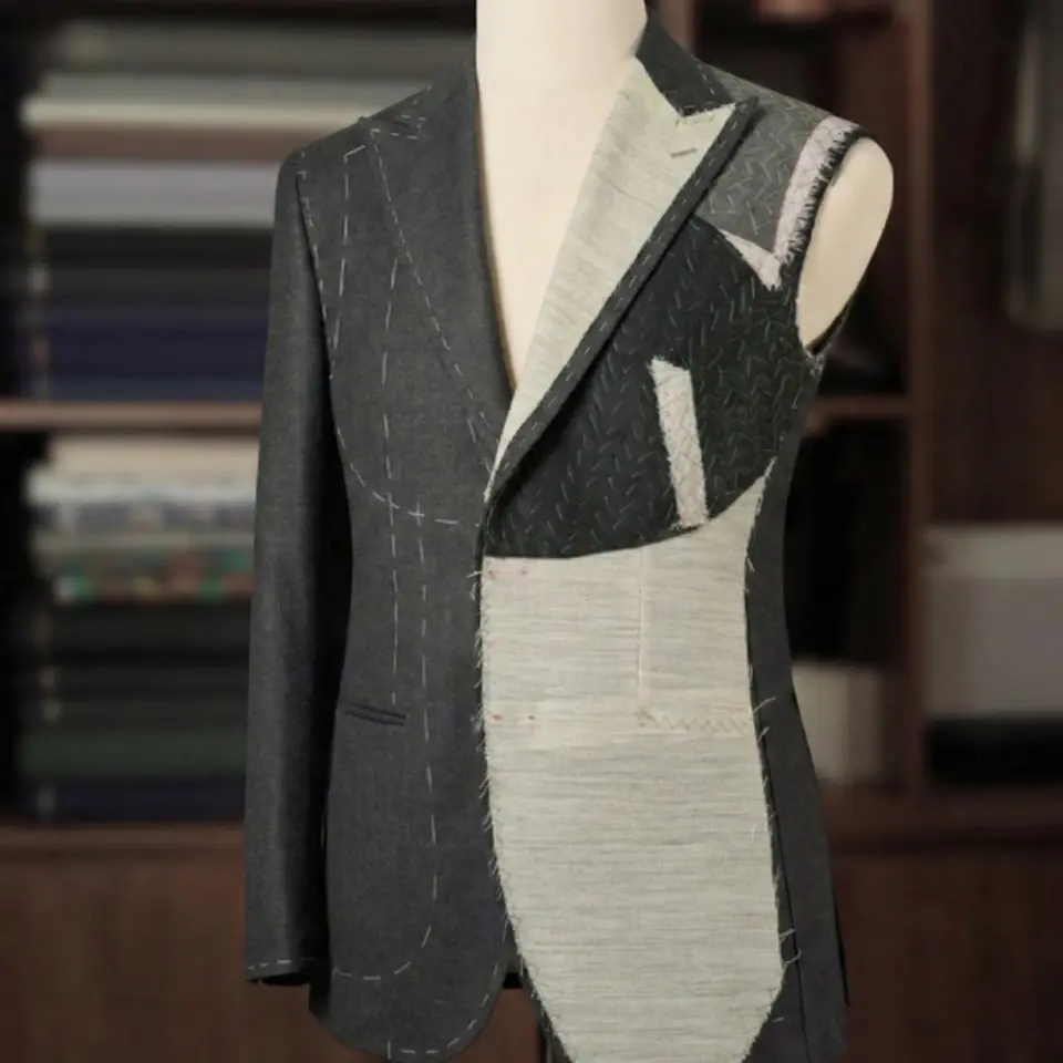 Half-constructed tailored suit on mannequin in a workroom, showing stitching and fabric layers.