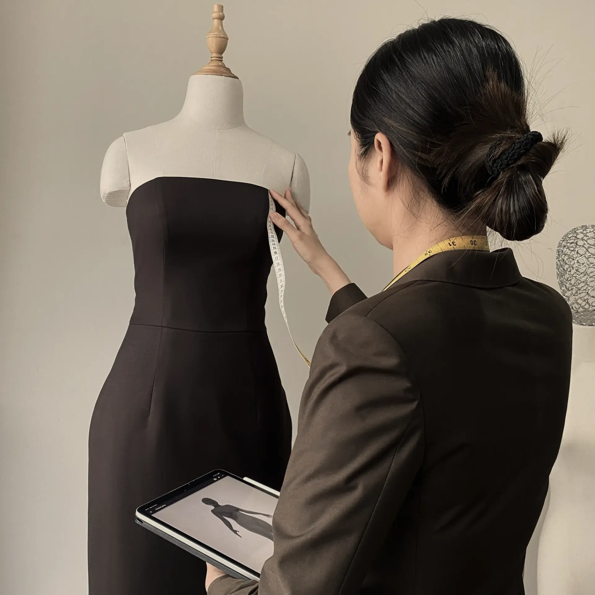 Fashion designer measuring dress on mannequin with tape and tablet.