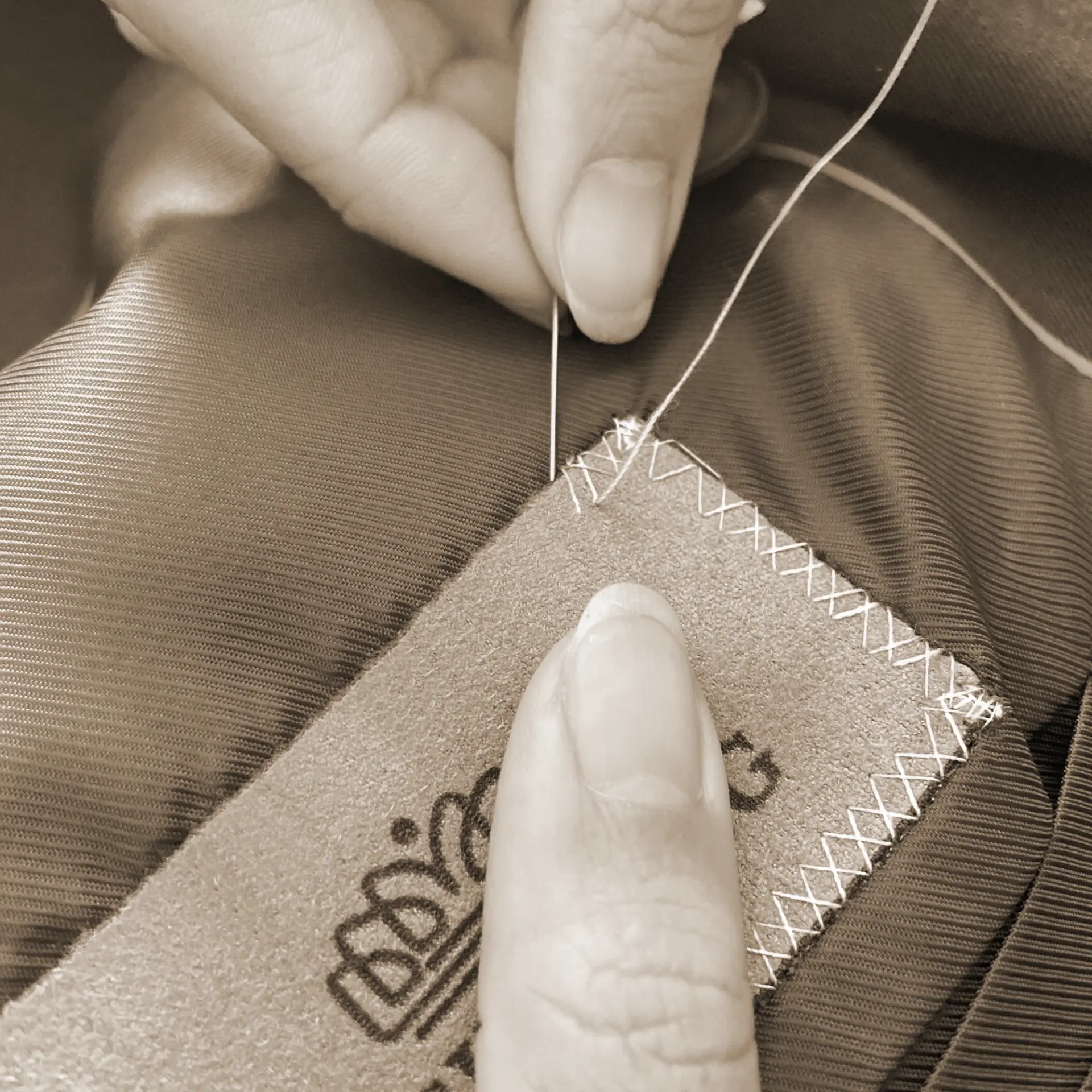 Close-up of hand stitching a label onto fabric, showcasing detailed needlework in a vintage style setting.