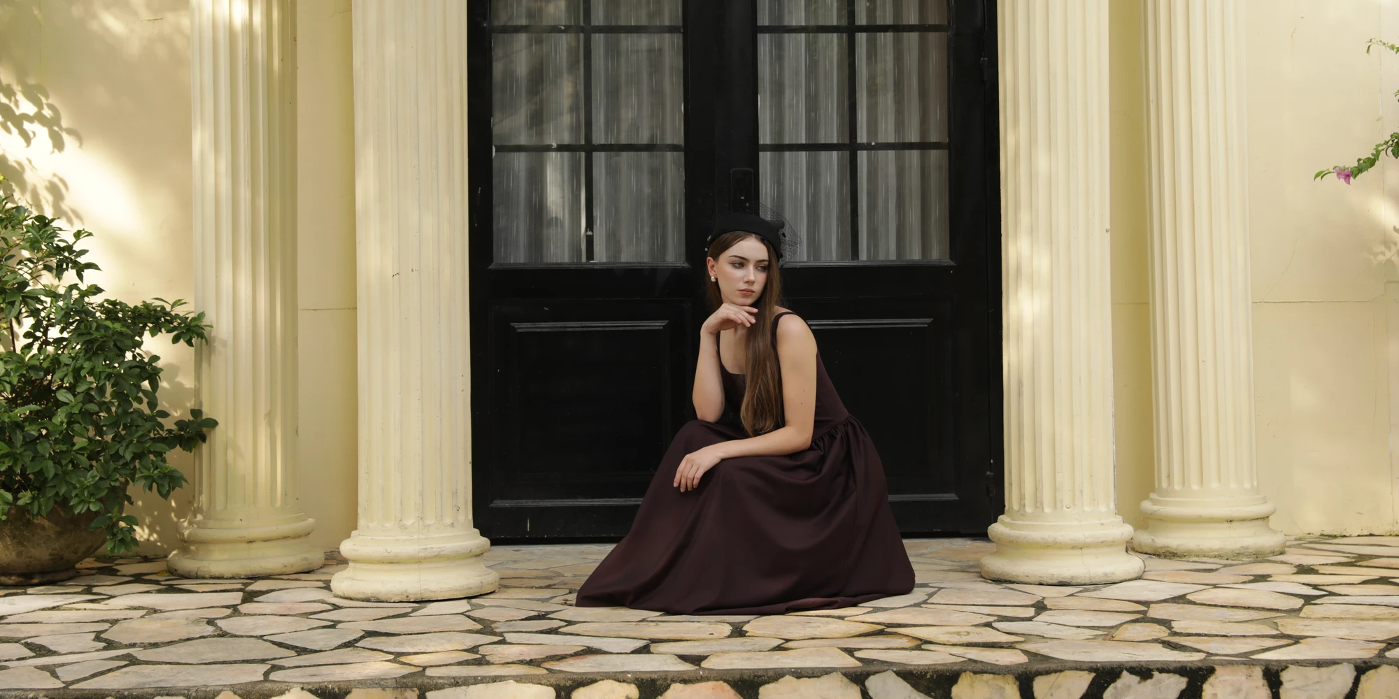 Woman in an elegant dress sits on steps outside a classic building with columns.