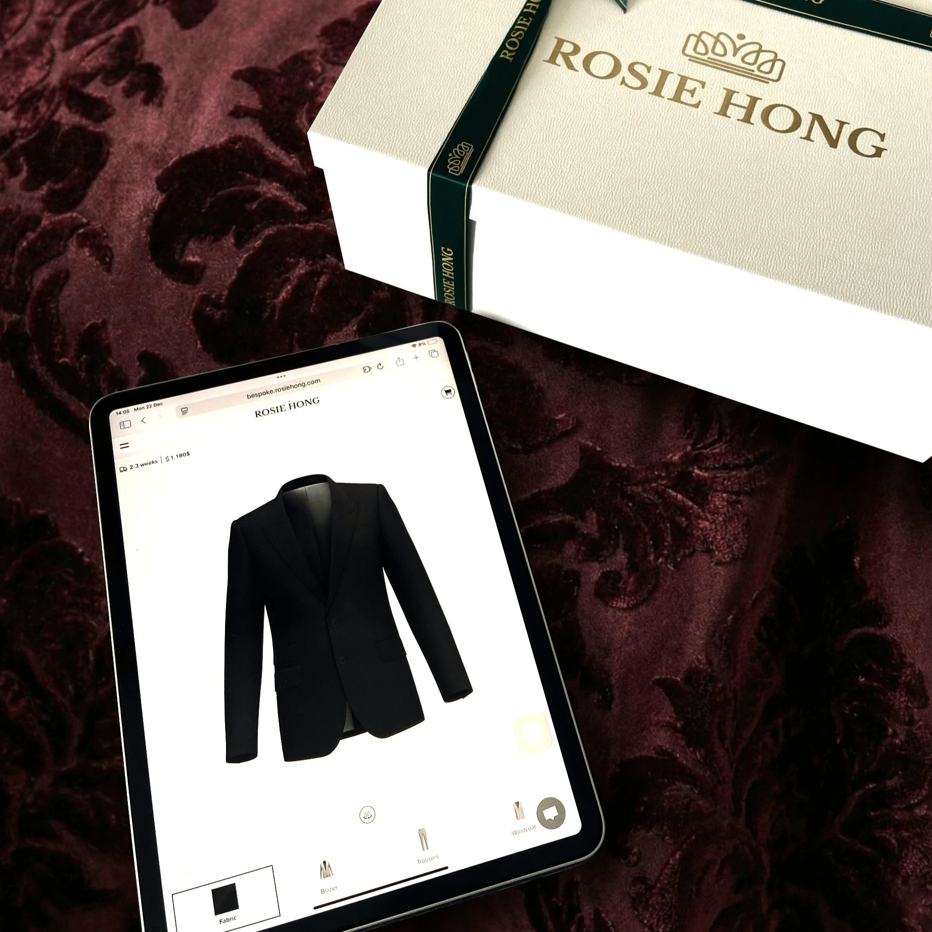 Tablet displaying a black suit jacket next to Rosie Hong branded box on a velvet surface.