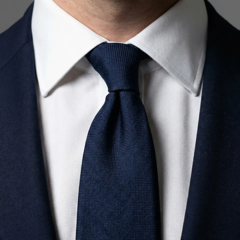 Close-up of a blue tie with a white shirt and dark blazer, showcasing a formal business attire detail.