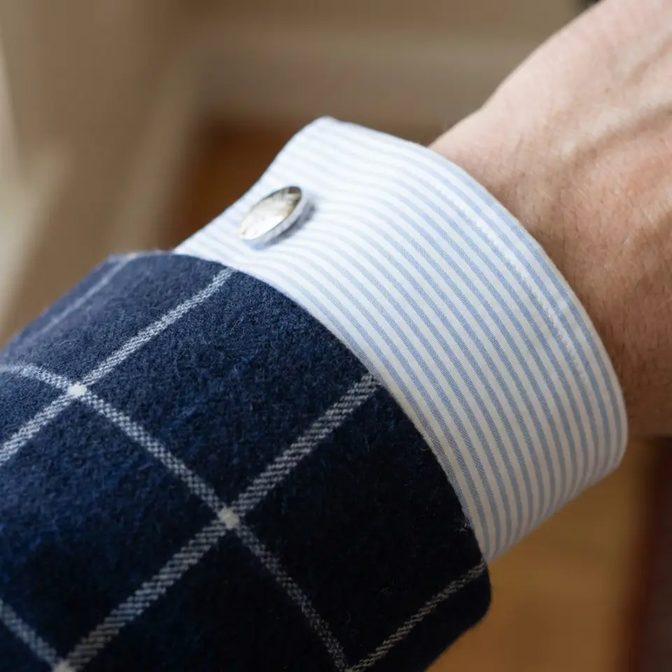 Blue checkered blazer sleeve with striped shirt cuff and silver button detail.
