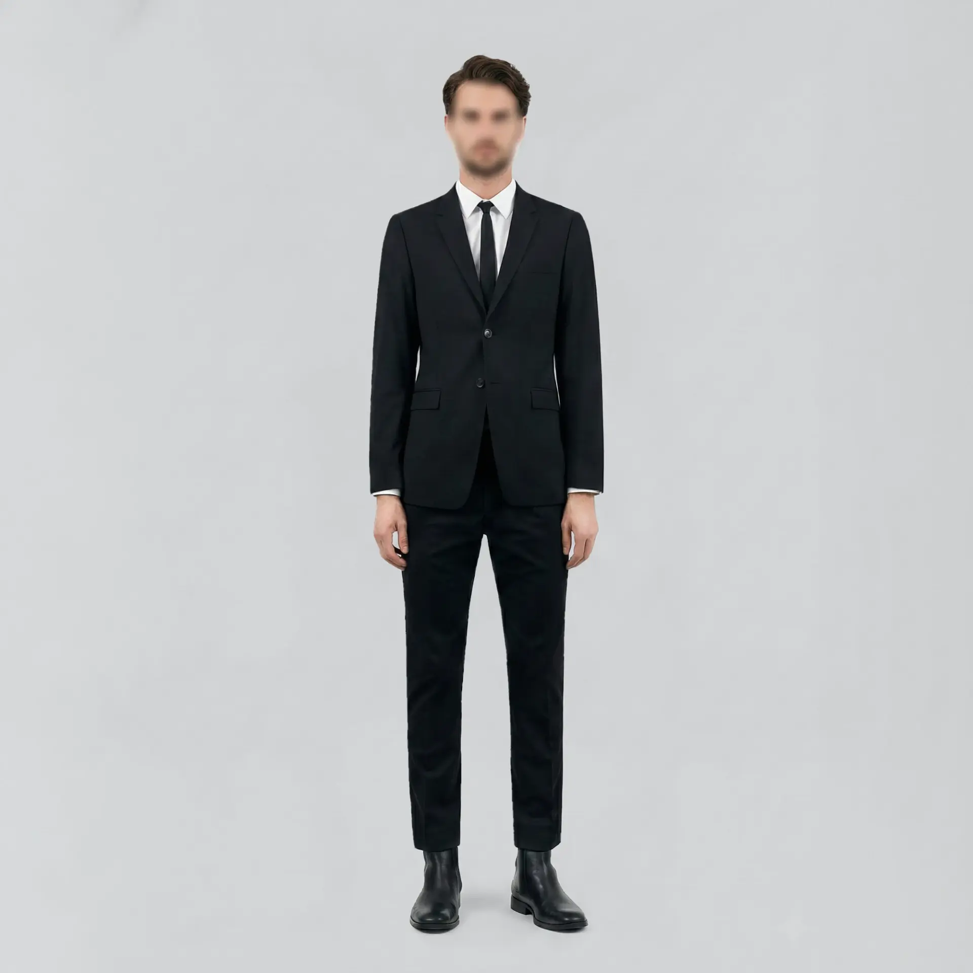Man in a tailored black suit, white shirt, and black tie, standing against a light gray background.