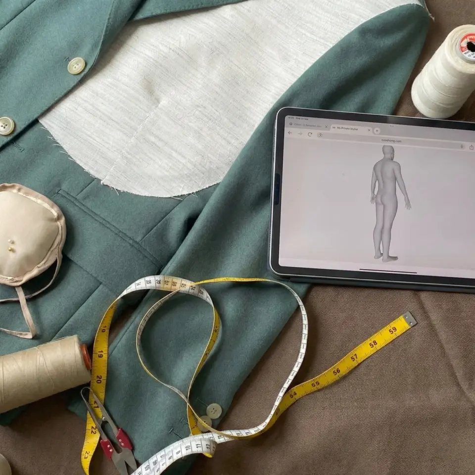 Tailor workspace with jacket, tape measure, tablet, and sewing tools for custom fitting and design.