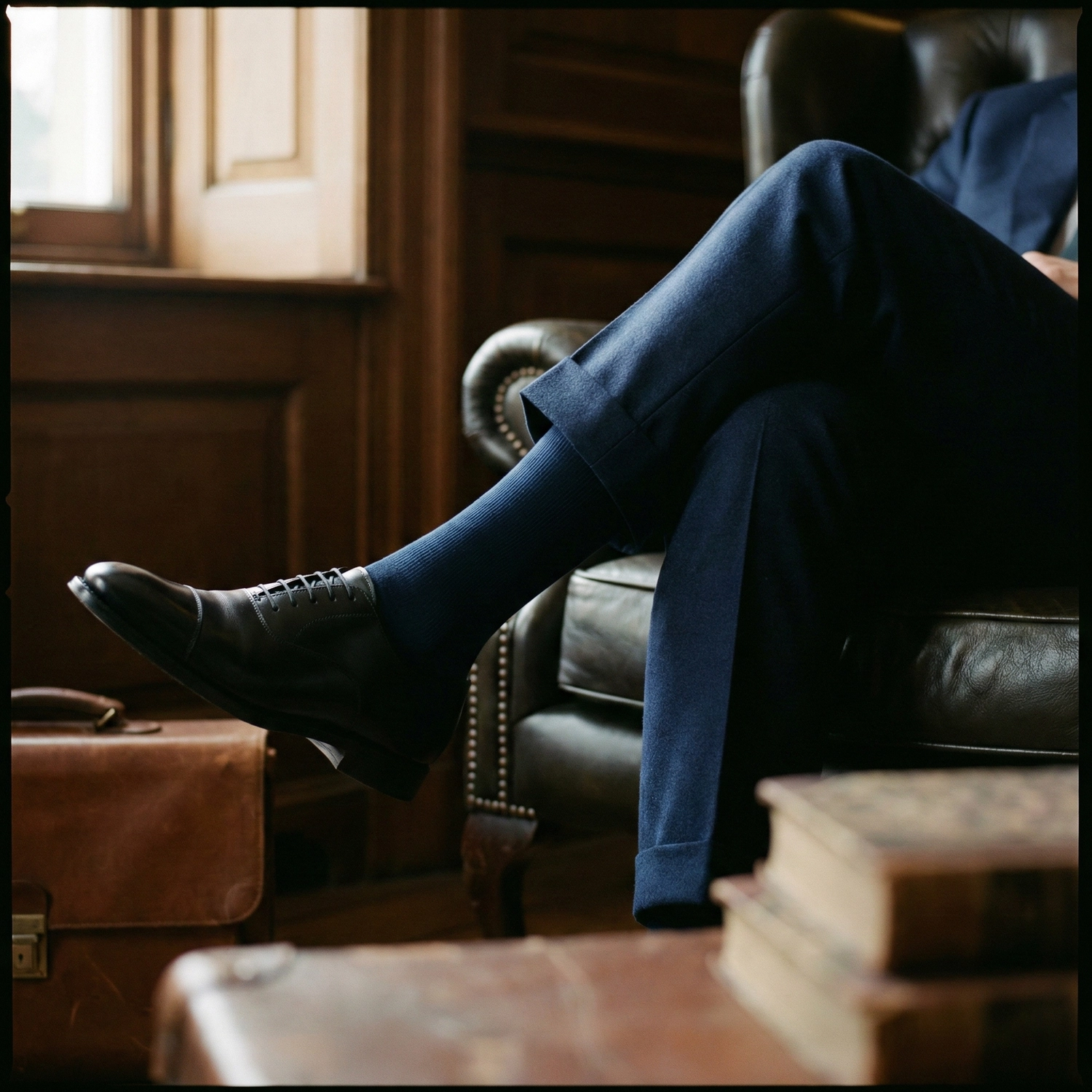 Man sitting with crossed legs wearing navy blue over-the-calf socks and black dress shoes